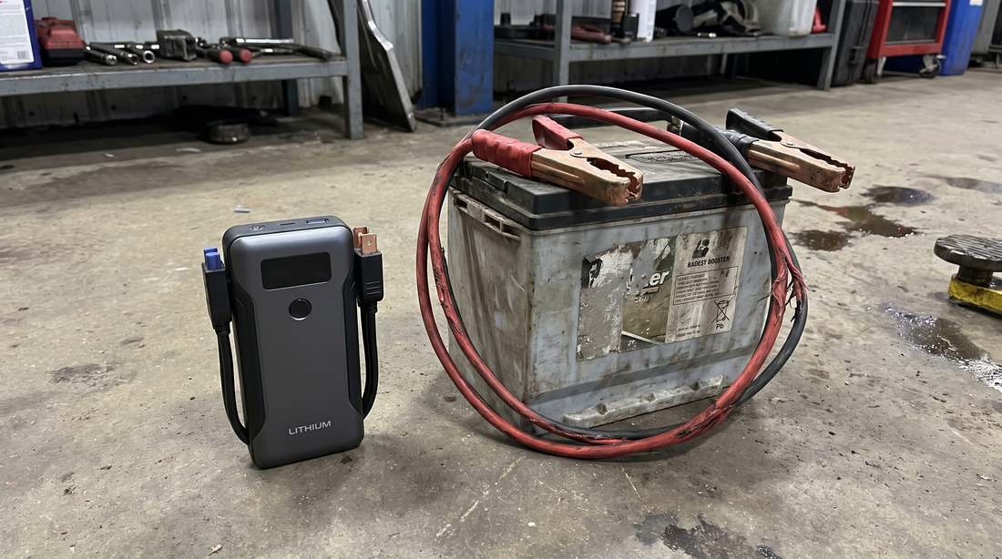 Compacte lithium jumpstarter naast grote oude loodzuur startbooster met accukabels op werkplaatsvloer